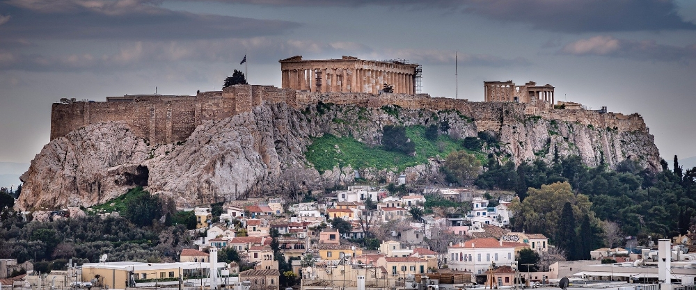 The hill of the Acropolis of Athens with the illuminated Parthenon standing out against the city's urban landscape.